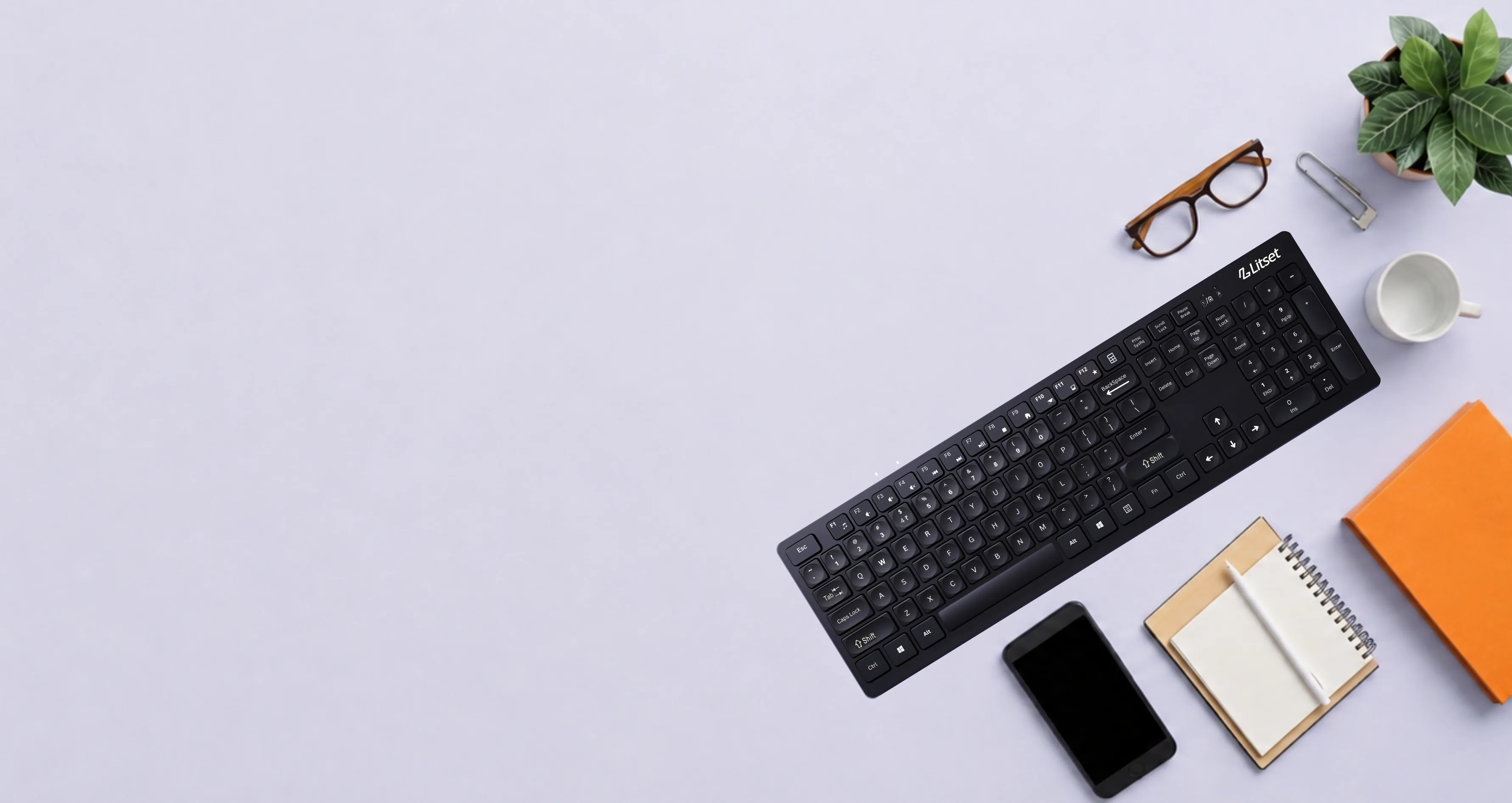 Litset wireless keyboard on a desk with glasses, a notebook, phone, and a plant